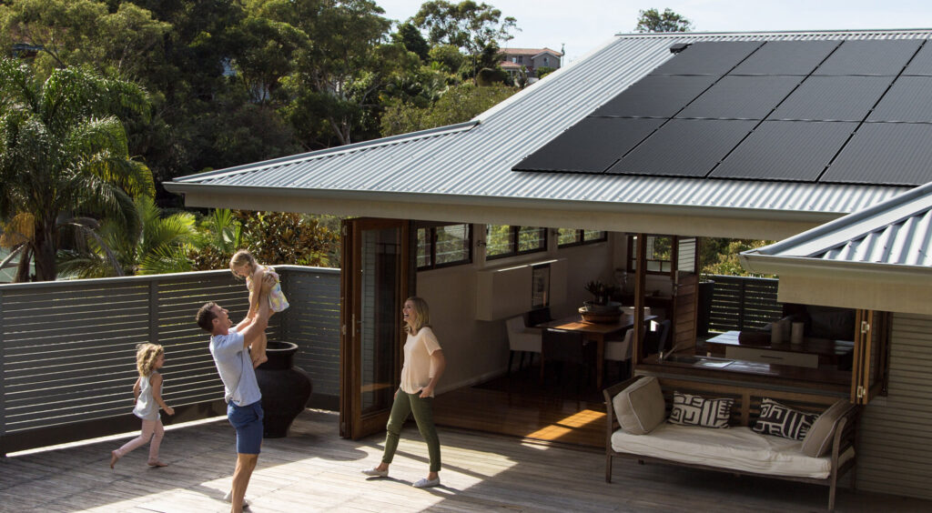 A man holding a baby on his shoulders in front of a house with Solahart Silhouette Solar panels